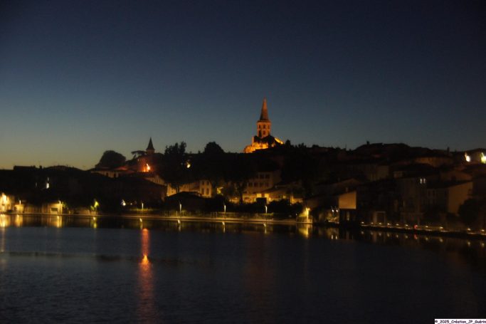 Le midi Somptueux Vue nocturne d'une ville avec des lumières réfléchies sur l'eau et une tour éclairée.